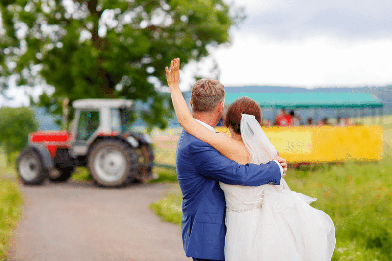 Bride and groom waving at guests in a tractor wedding venue transport
